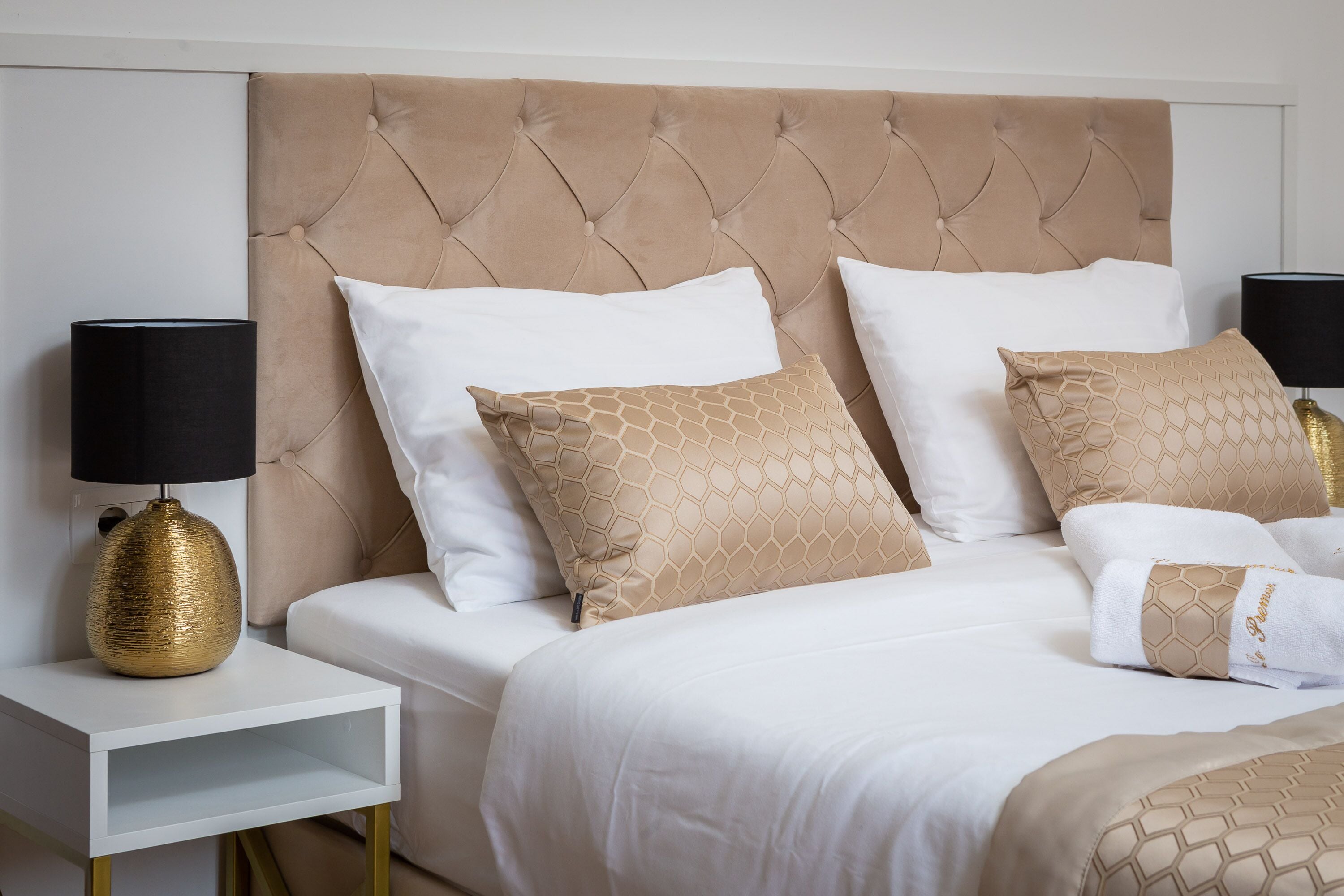 A bed with a tufted headboard, white bedding, and patterned pillows.