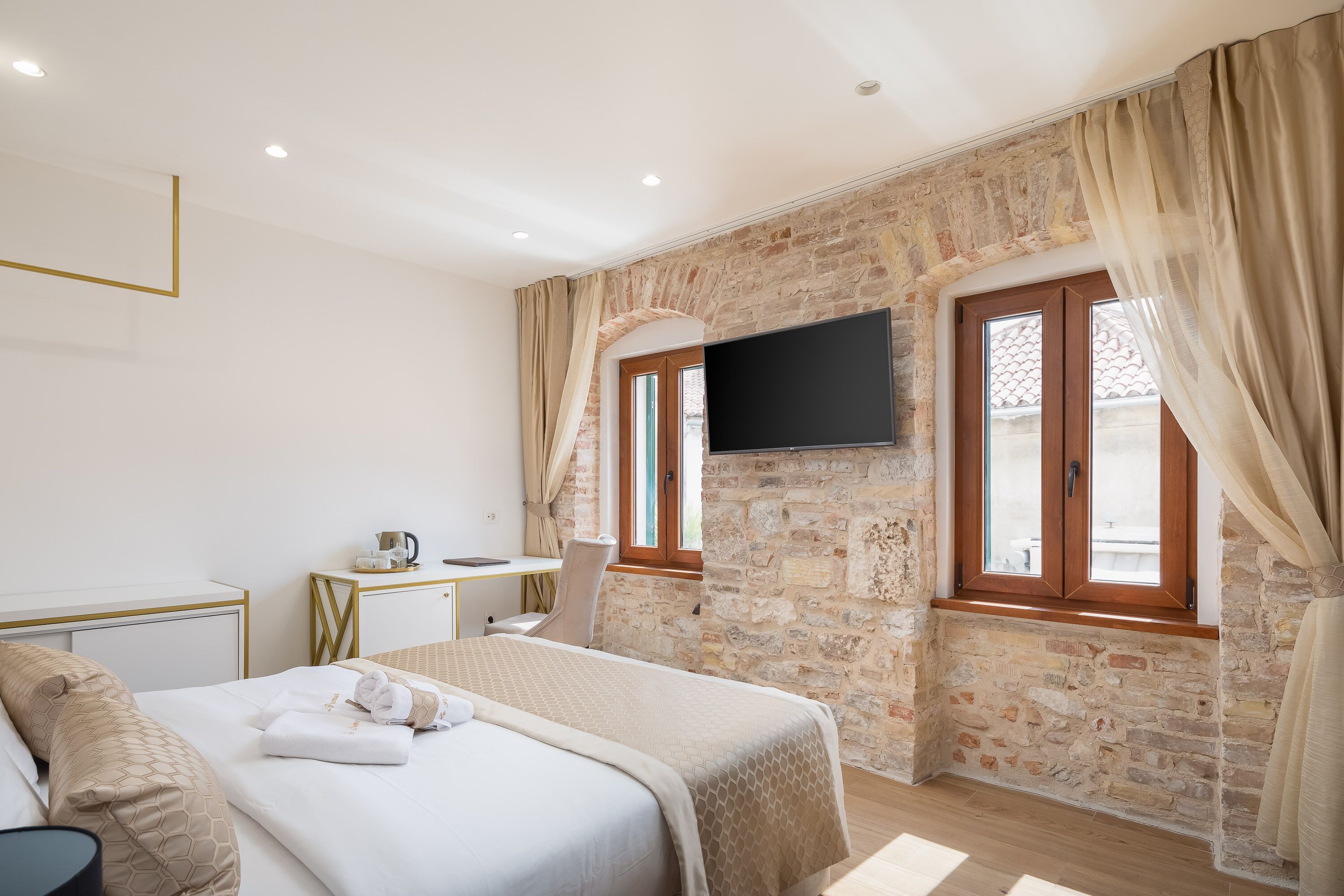 Une chambre avec un lit, un bureau, une chaise, une télévision et un mur en pierre.