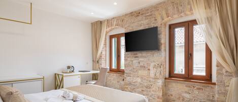 Une chambre avec un lit, un bureau, une chaise, une télévision et un mur en pierre.