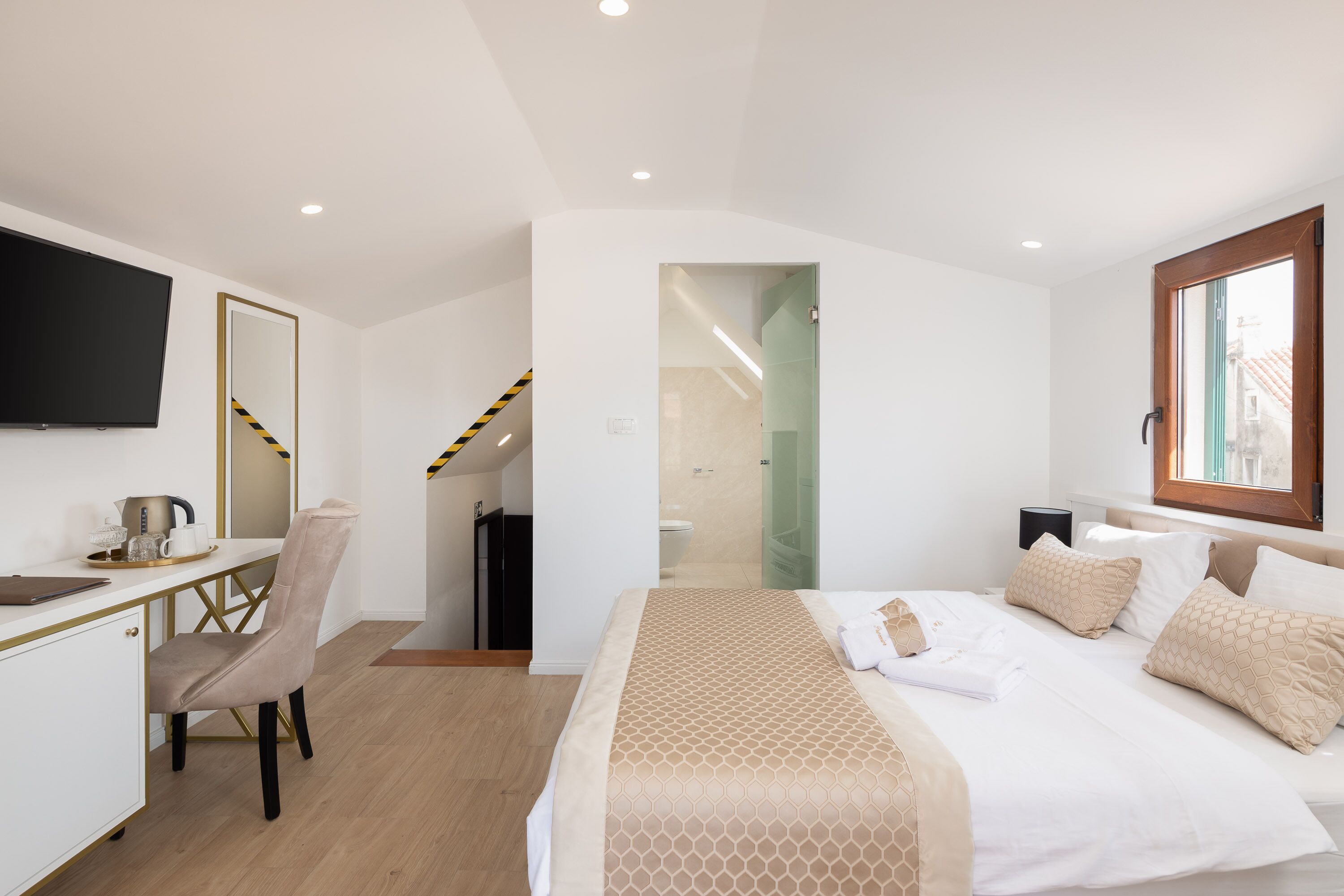 Habitación de hotel con cama, escritorio, silla, televisión y baño visible a través de una puerta abierta.