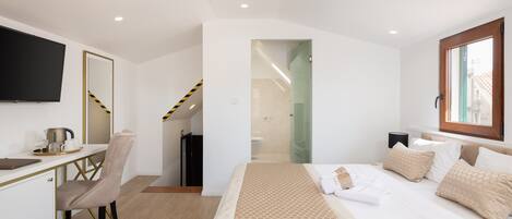 Habitación de hotel con cama, escritorio, silla, televisión y baño visible a través de una puerta abierta.