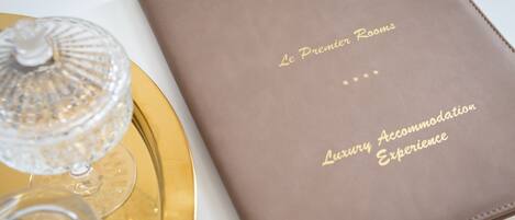 A brown leather-bound booklet with gold embossed text reading "Le Premier Rooms Luxury Accommodation Experience."
