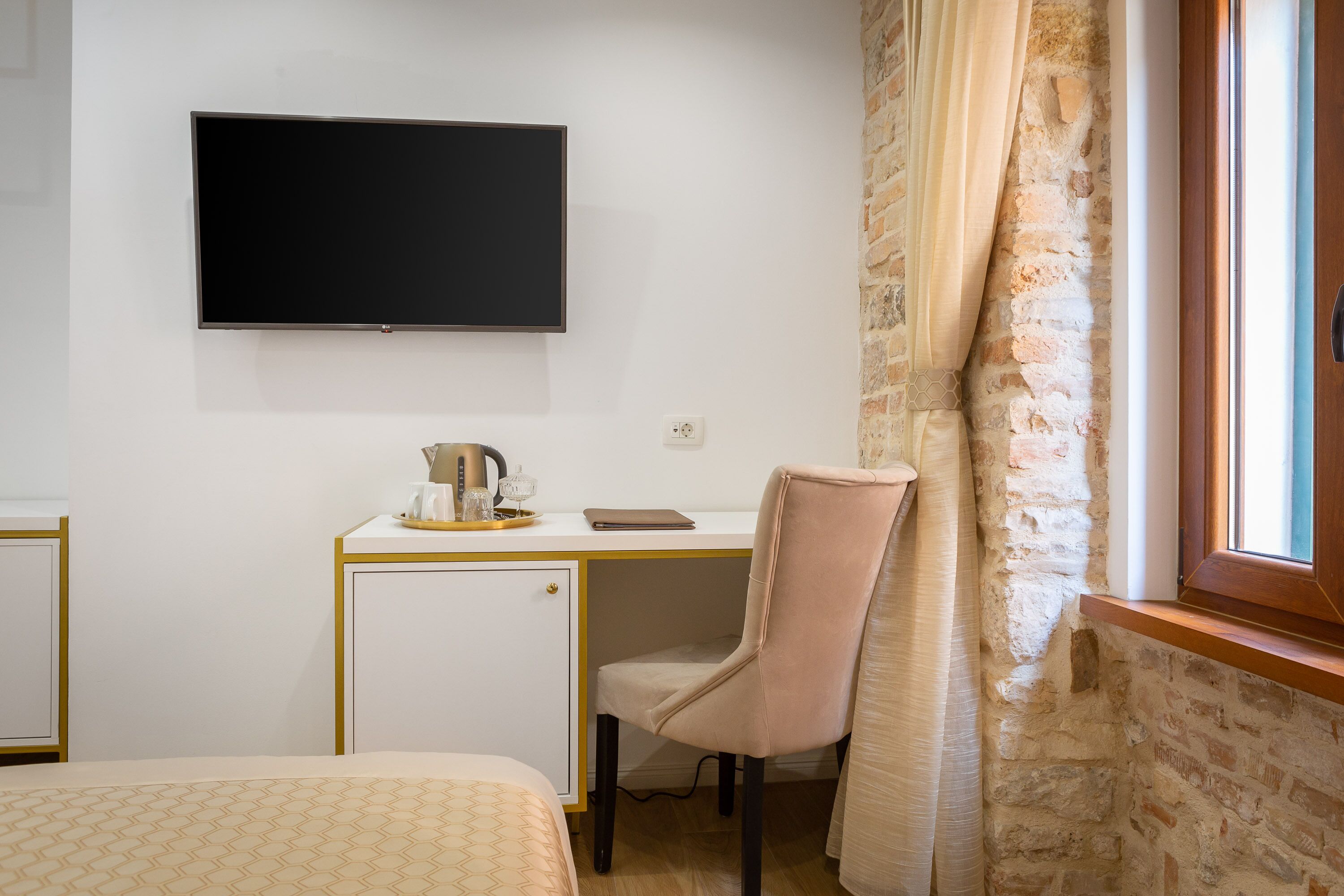 Habitación de hotel con una cama, un escritorio con televisor, un refrigerador pequeño y una ventana con cortinas.