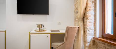 Habitación de hotel con una cama, un escritorio con televisor, un refrigerador pequeño y una ventana con cortinas.