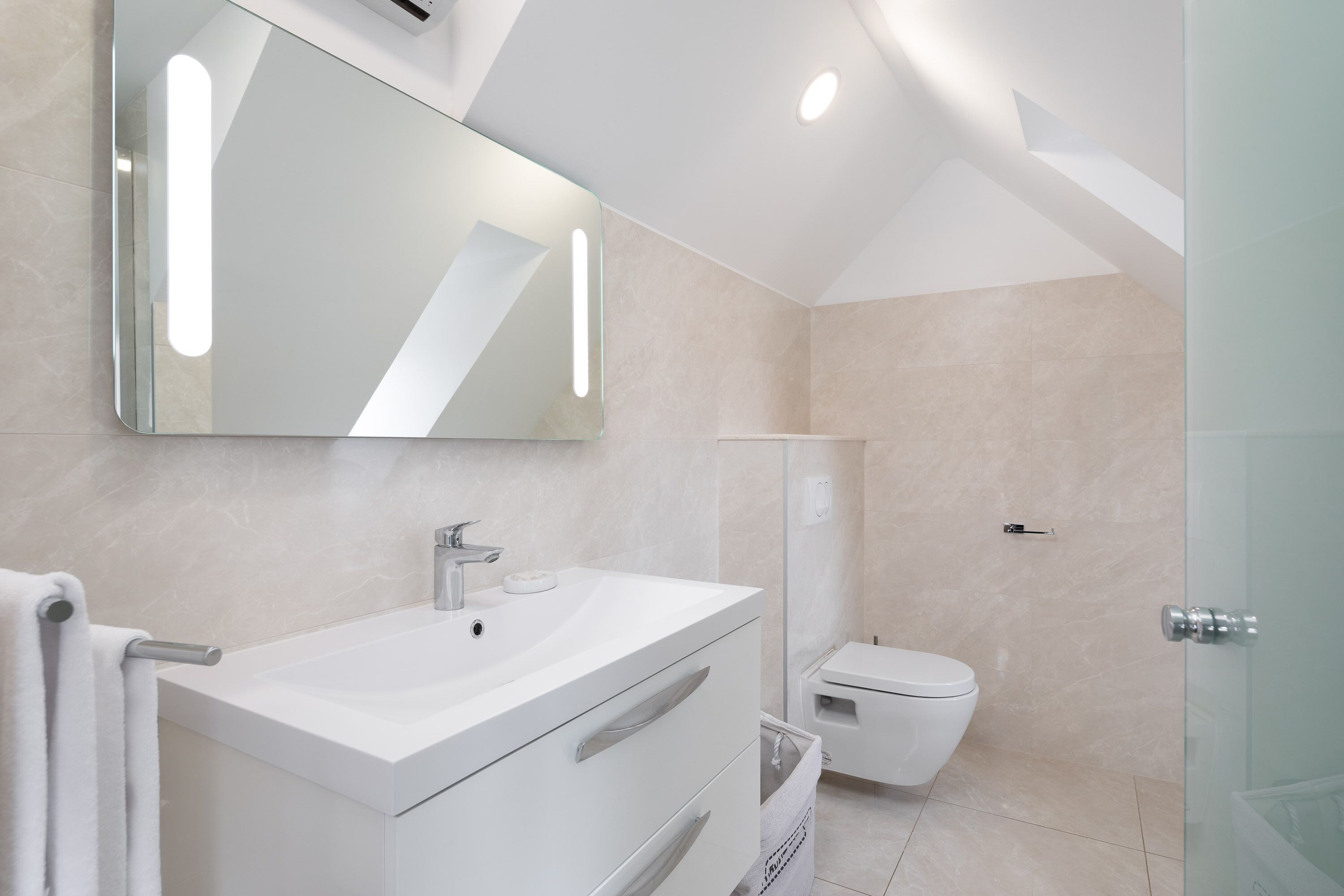 Une salle de bain moderne avec un meuble-lavabo blanc, un grand miroir, des toilettes et une douche à parois de verre.