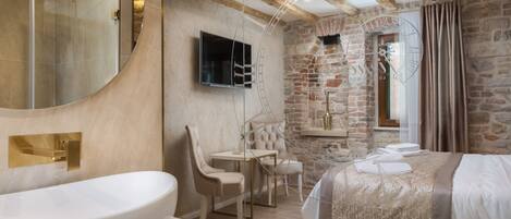 Una habitación de hotel moderna con un lavamanos ovalado grande, una cama con colcha estampada, un televisor montado en la pared y una pared de piedra.