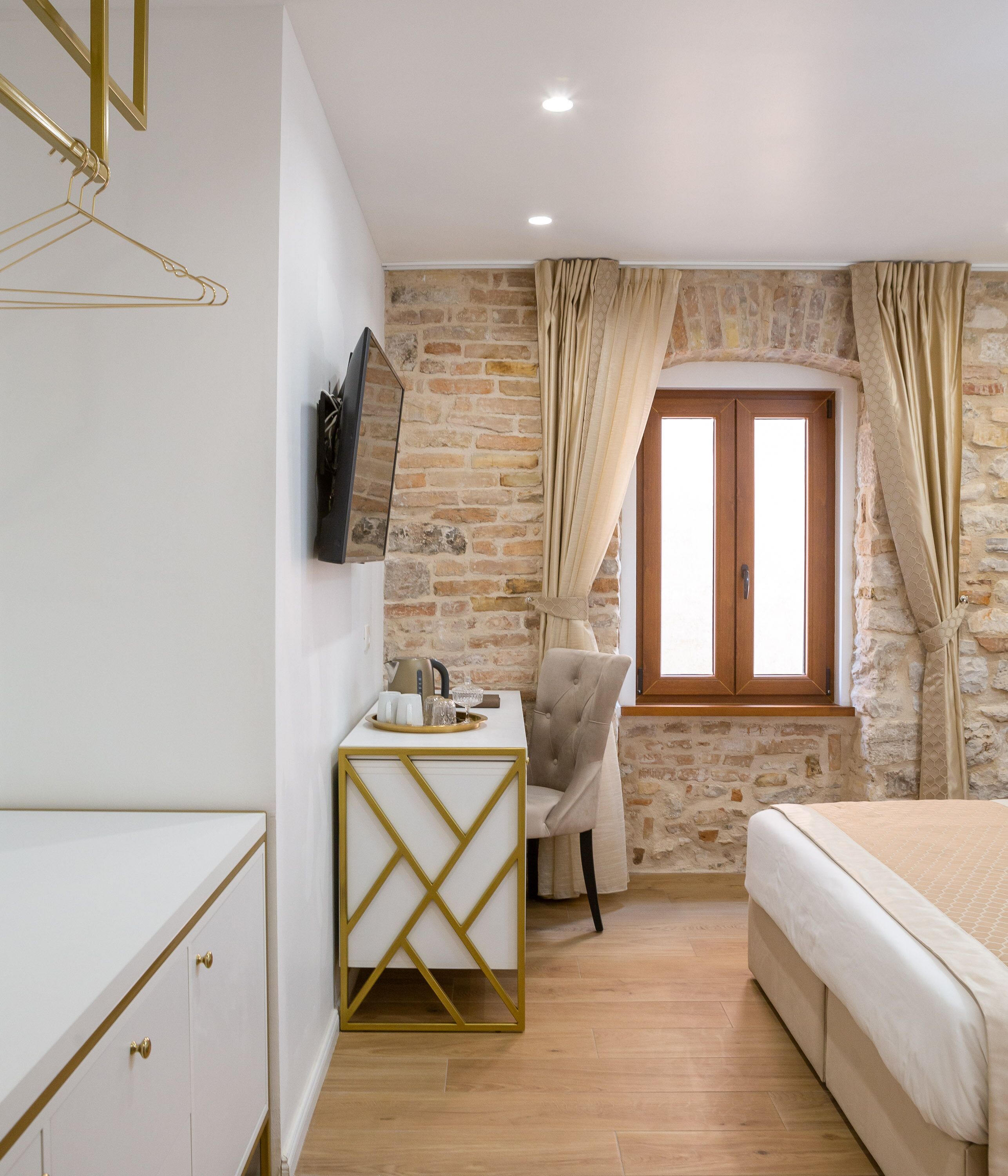 Un dormitorio con cama, un escritorio con silla, un televisor montado en la pared y una pared de piedra.