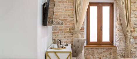 Un dormitorio con cama, un escritorio con silla, un televisor montado en la pared y una pared de piedra.