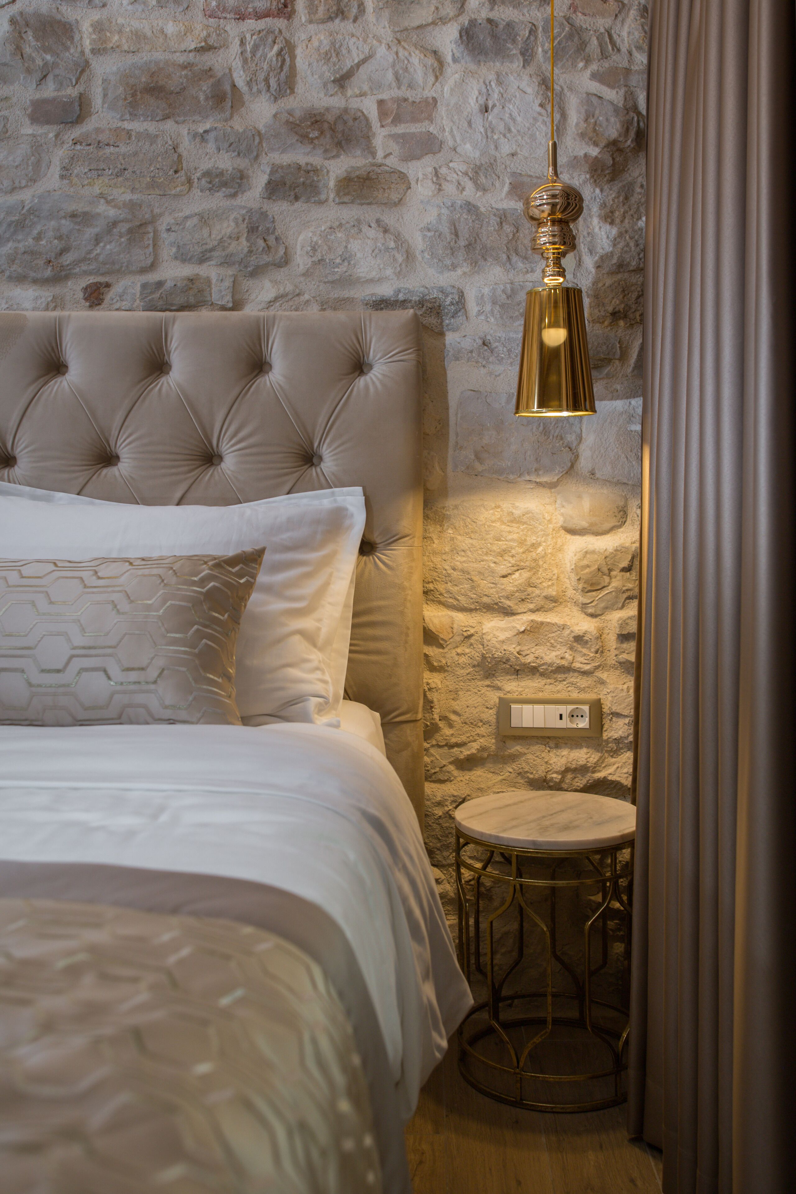 A bedroom with a tufted headboard, a round side table, and a hanging light fixture.
