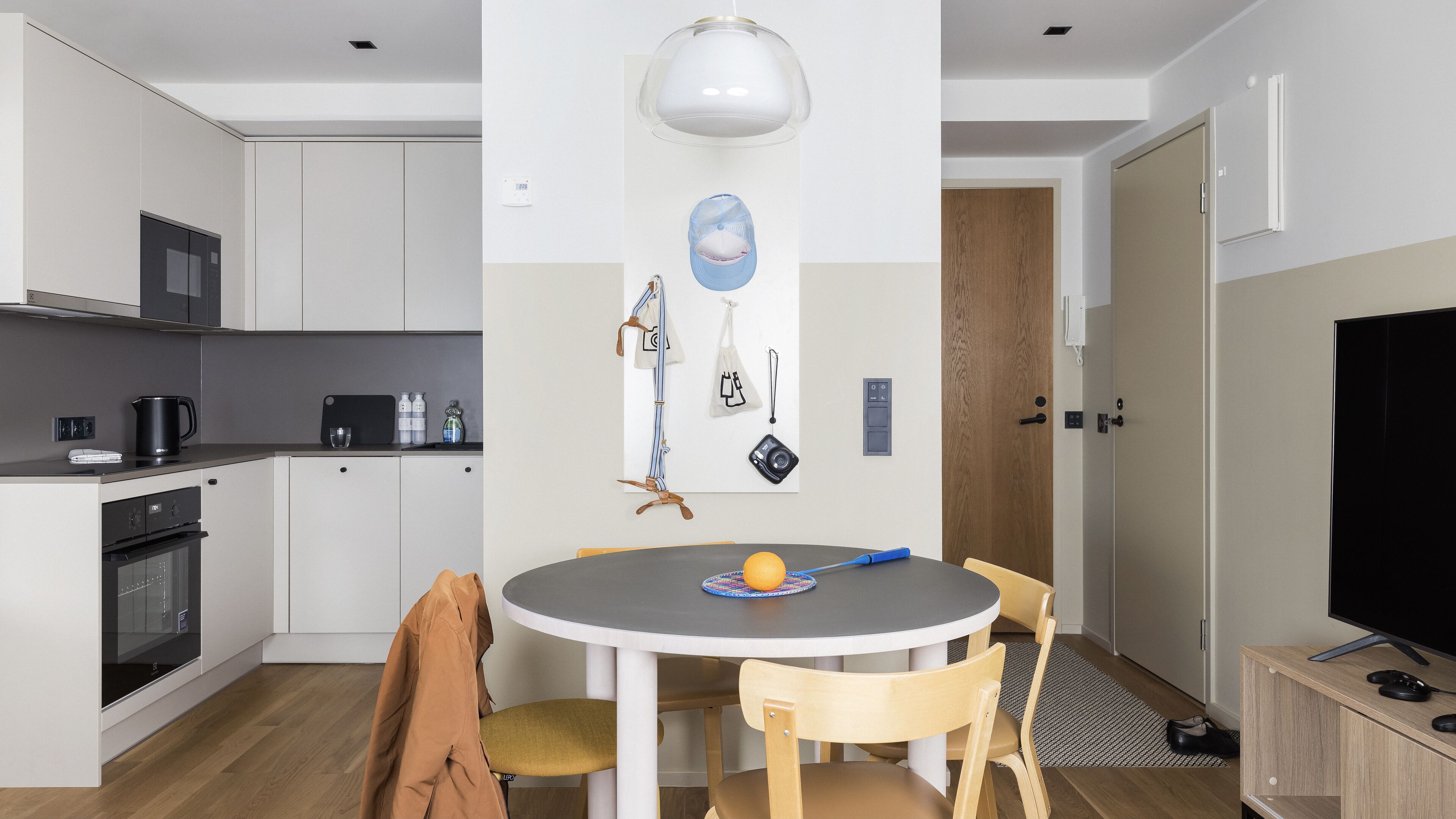 A modern kitchen with white cabinets, a microwave, and a coffee maker. There is a dining area with a round table, chairs, and a TV.