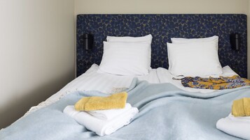 Un letto rifatto con lenzuola bianche, una testiera azzurra a motivi decorativi e due lampade fissate alla parete.