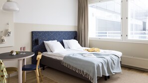 A hotel room with a bed, a small table, a chair, and a window with a view of buildings. - Bob W Helsinki City Centre (Helsinki)