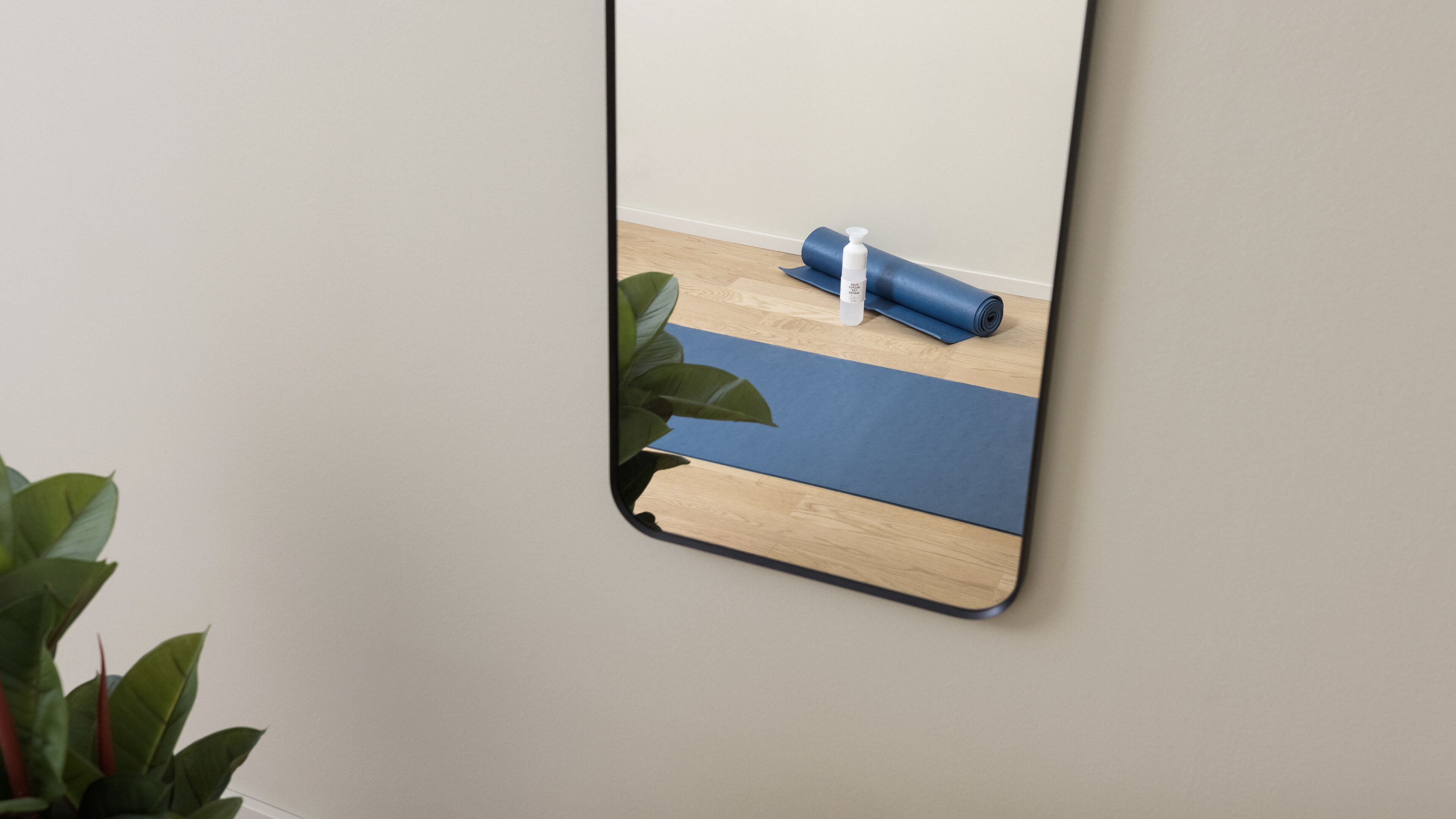 A mirror reflecting a yoga mat and a bottle on a wooden floor.