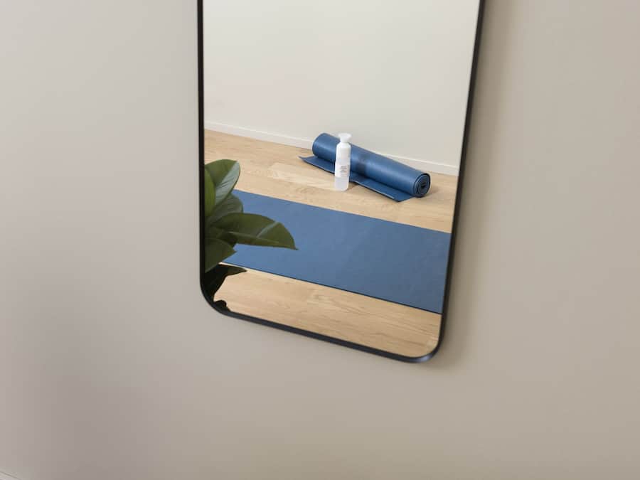 A mirror reflecting a yoga mat and a bottle on a wooden floor.
