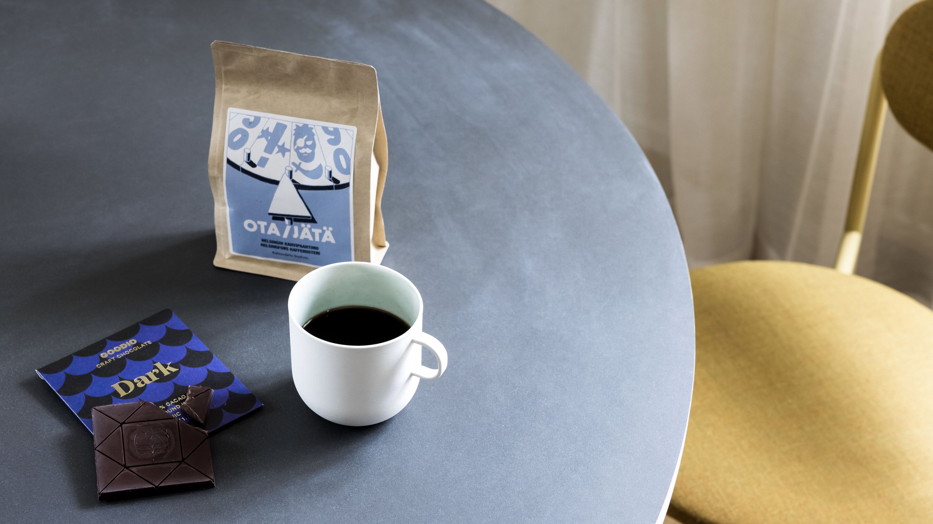 A table with a coffee cup, a chocolate bar, and a coffee bag.