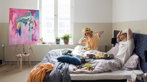 A hotel room with a bed, a painting on the wall, a window with a view, and a breakfast setup on the bed. - Bob W Helsinki City Centre (Helsinki)