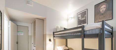 A bunk bed room with a desk, a trash bin, and a door.