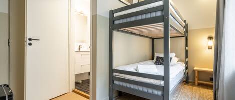 A bunk bed room with a door, a bathroom, and a small bench.