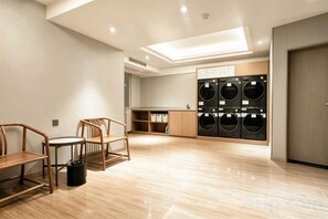 Een wasserette met meerdere wasmachines, houten stoelen, een tafel en een prullenbak.