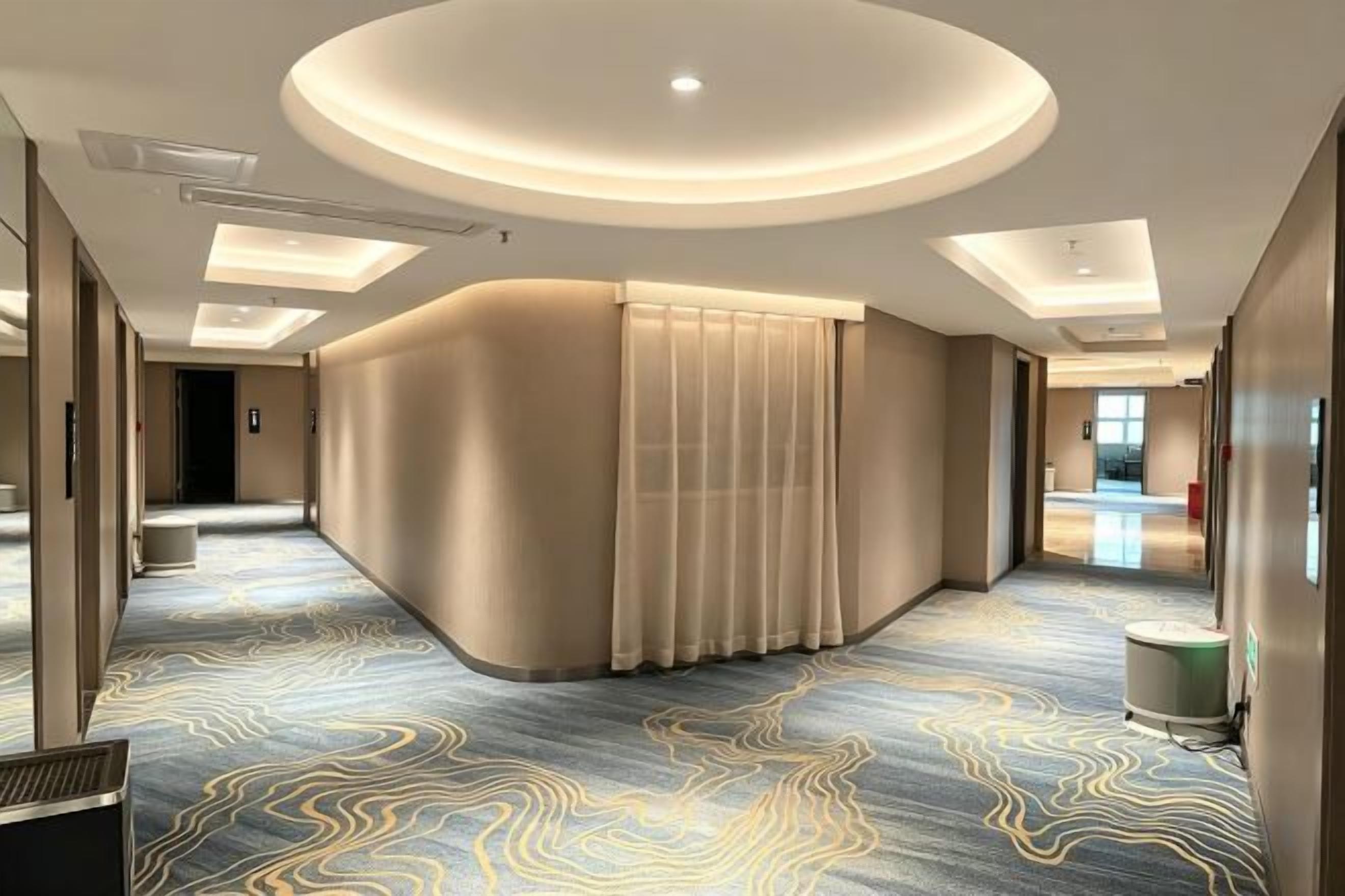 Et hotel lobby med en buet receptionsdisk, et mønstret tæppe og et moderne loftdesign.