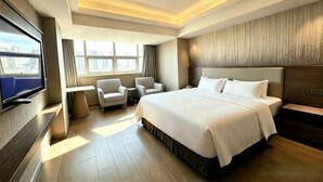 Ein Hotelzimmer mit einem großen Bett, einem Fernseher, einer Sitzecke mit Sesseln und Blick auf die Stadt.