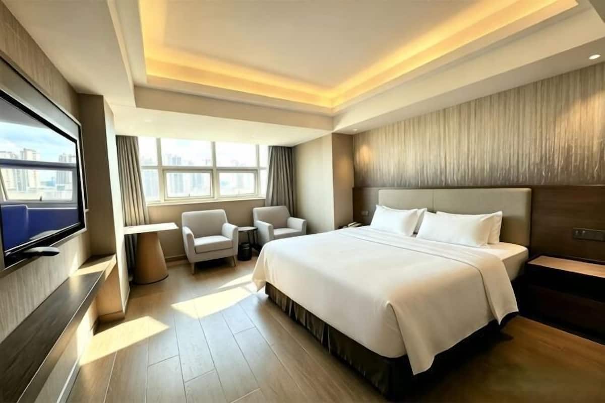 Een hotelkamer met een groot bed, een televisie, een zithoek met stoelen en uitzicht op de stad.