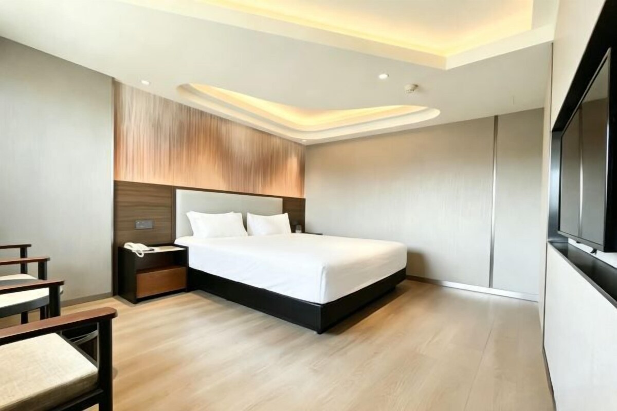 A modern hotel room with a large bed, bedside tables, a desk, and a TV.