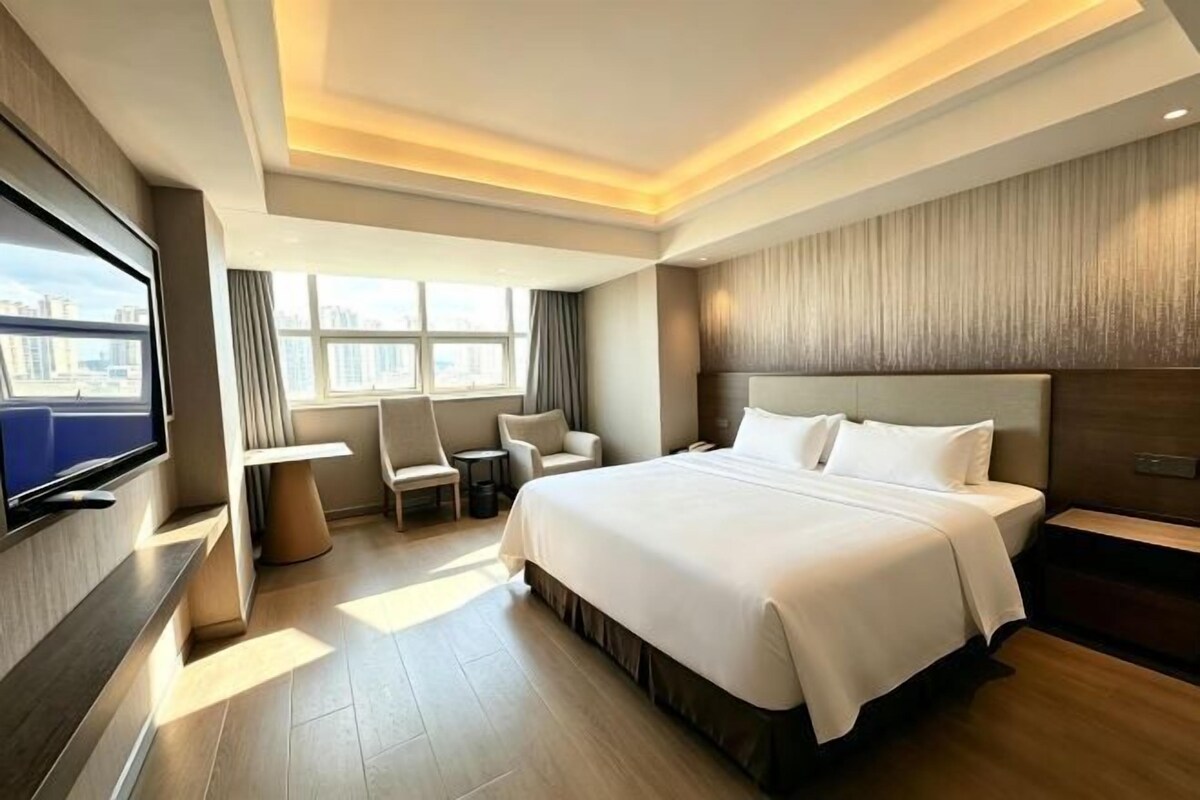 A hotel room with a large bed, a TV, a desk, and a view of the city.