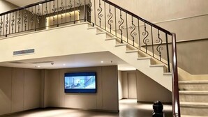 Eine großzügige Lobby mit hoher Decke, einem großen Flachbildfernseher, einer Treppe mit schmiedeeisernem Geländer und einem schwarzen Stuhl.