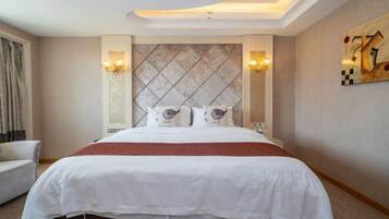 Una habitación de hotel con una cama grande, un cabecero con diseño de rombos, dos lámparas de pared y un cuadro en la pared.