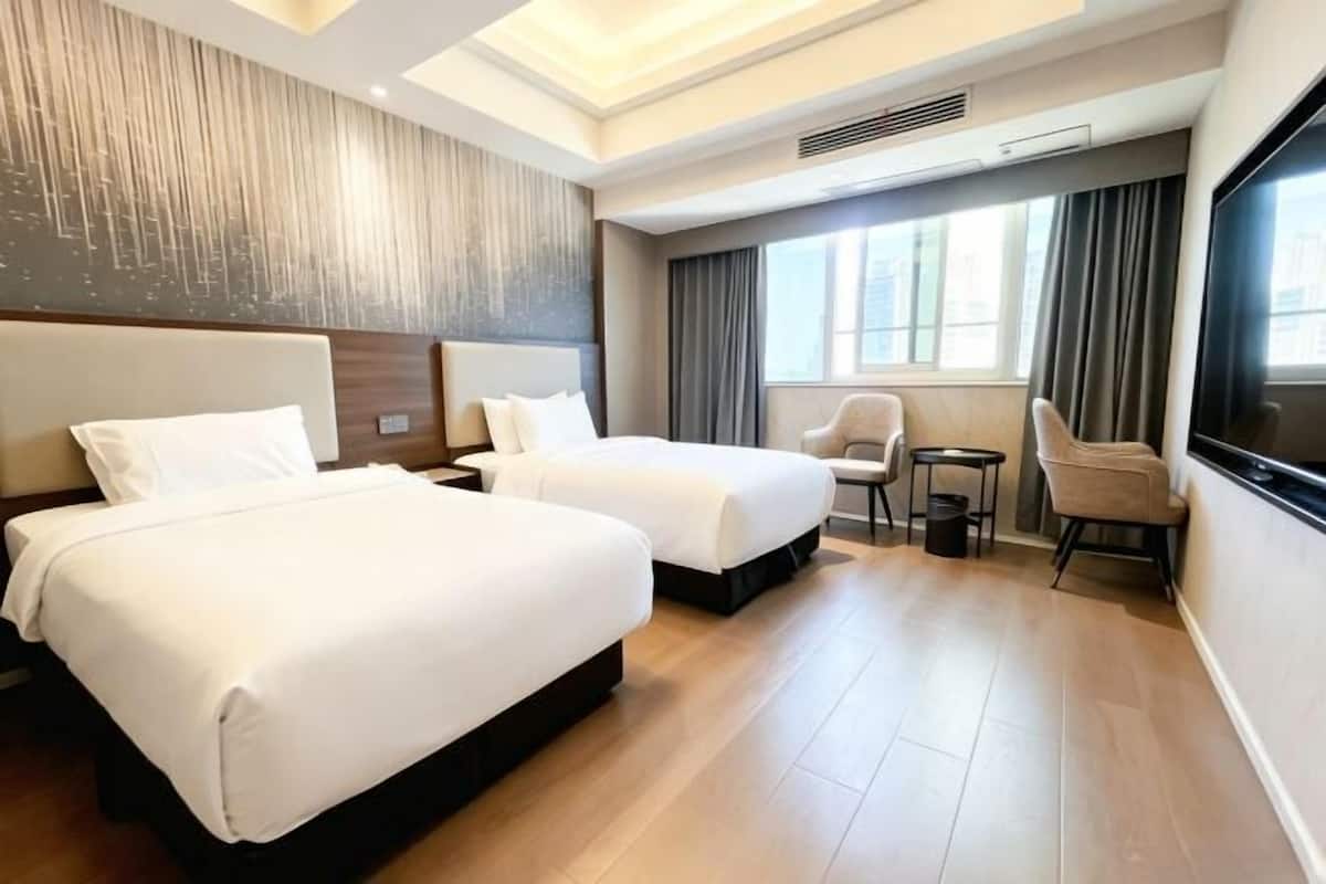Een hotelkamer met twee bedden, een tafeltje, een stoel en een groot raam.