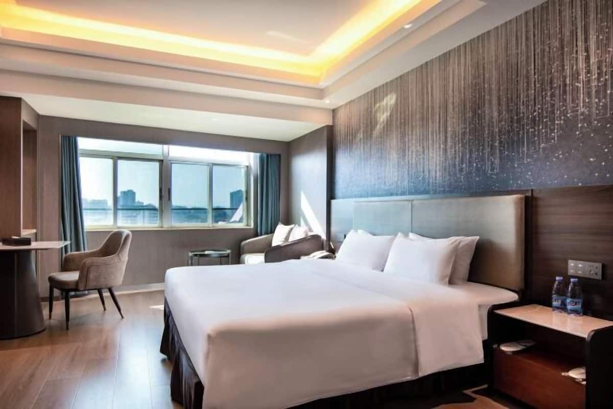 Habitación de hotel moderna con una cama grande, un escritorio y una silla. Se ve la ciudad a través de la ventana.