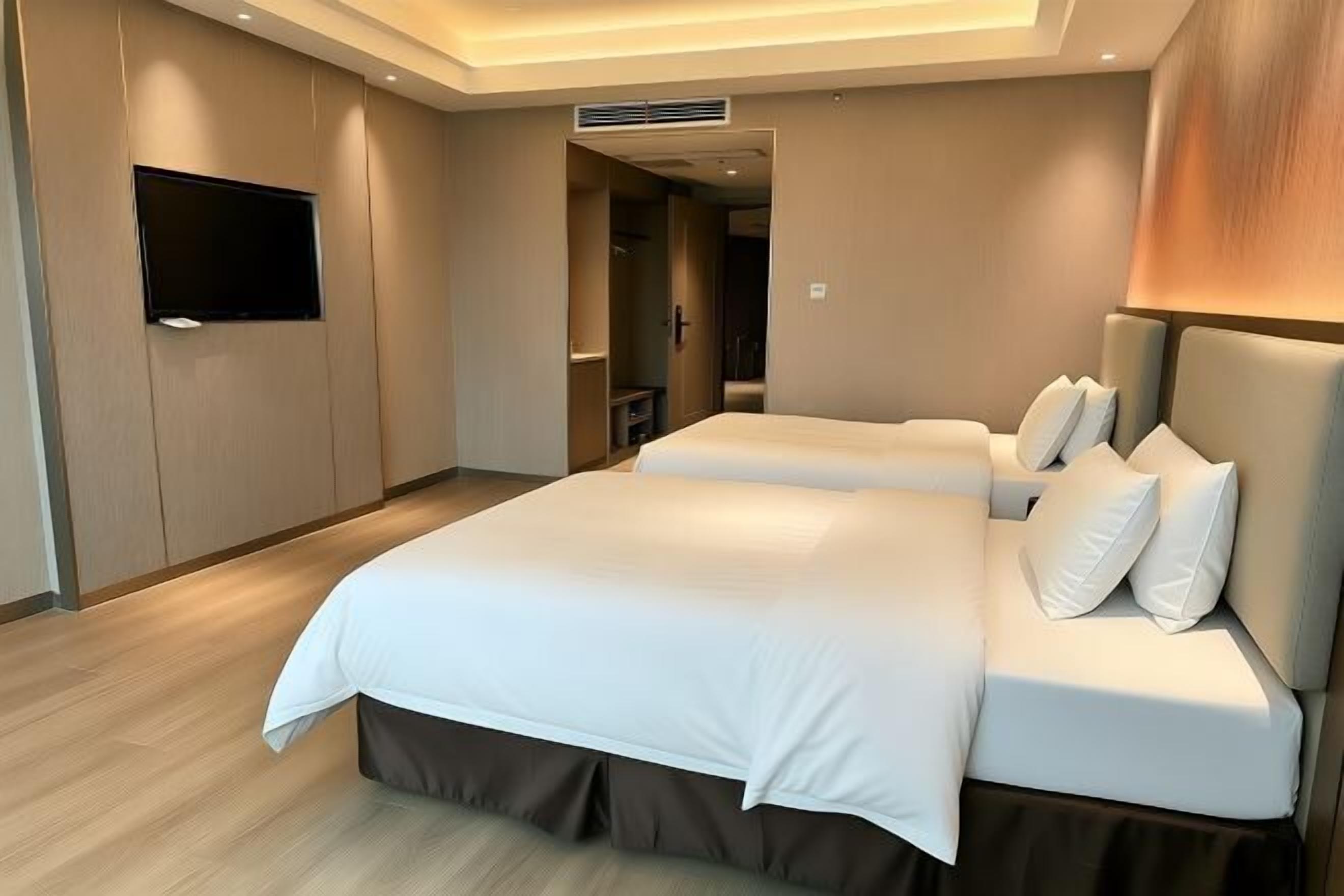 A hotel room with a large bed, a flat-screen TV, and a wooden floor.