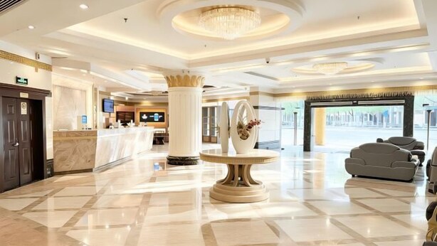 Eine Hotelhalle mit Marmorboden, einer Rezeption, einer großen Säule, einem runden Tisch mit Vase sowie einer Couch.