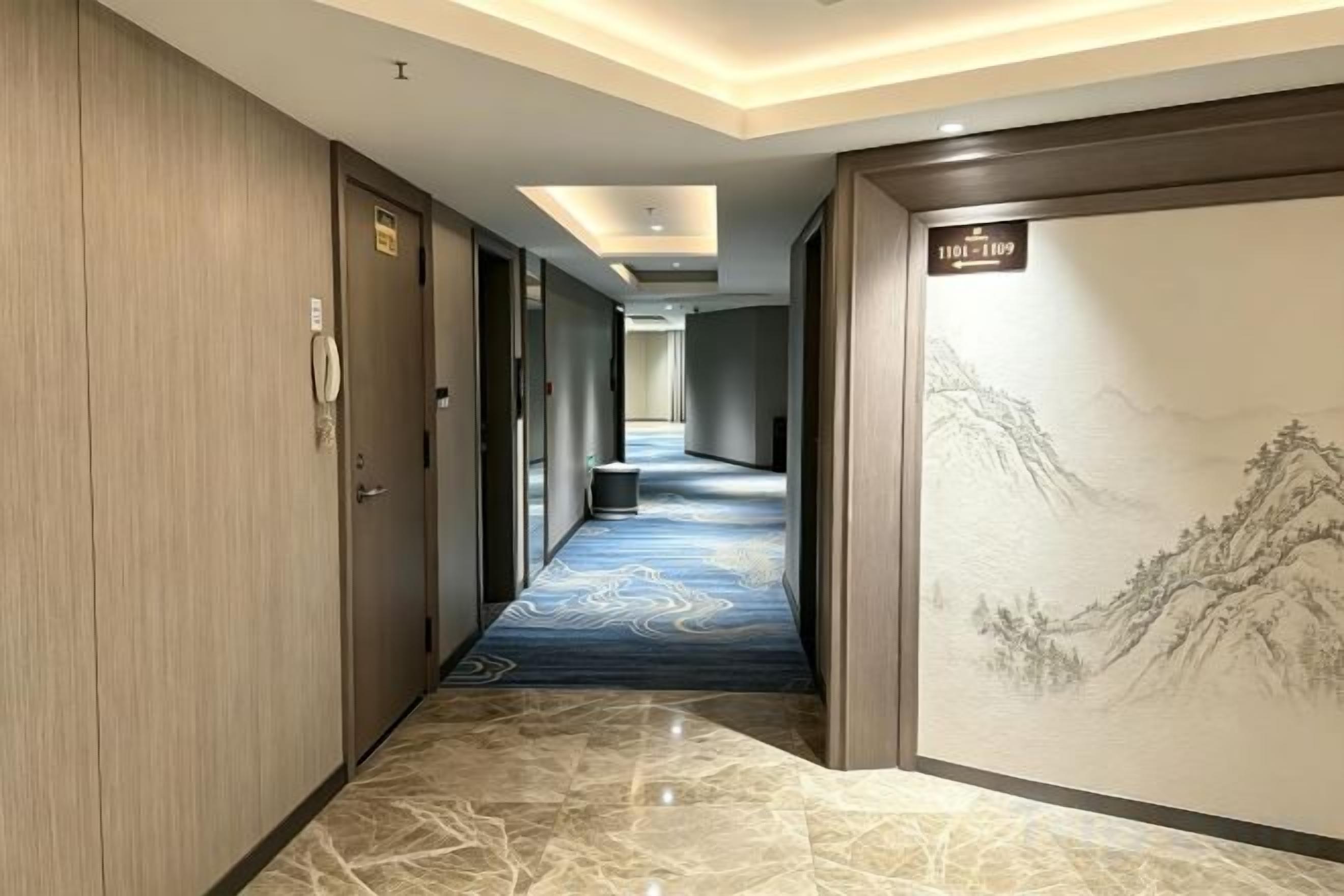 Un couloir d’hôtel avec un sol en marbre, des portes en bois et une grande peinture murale.