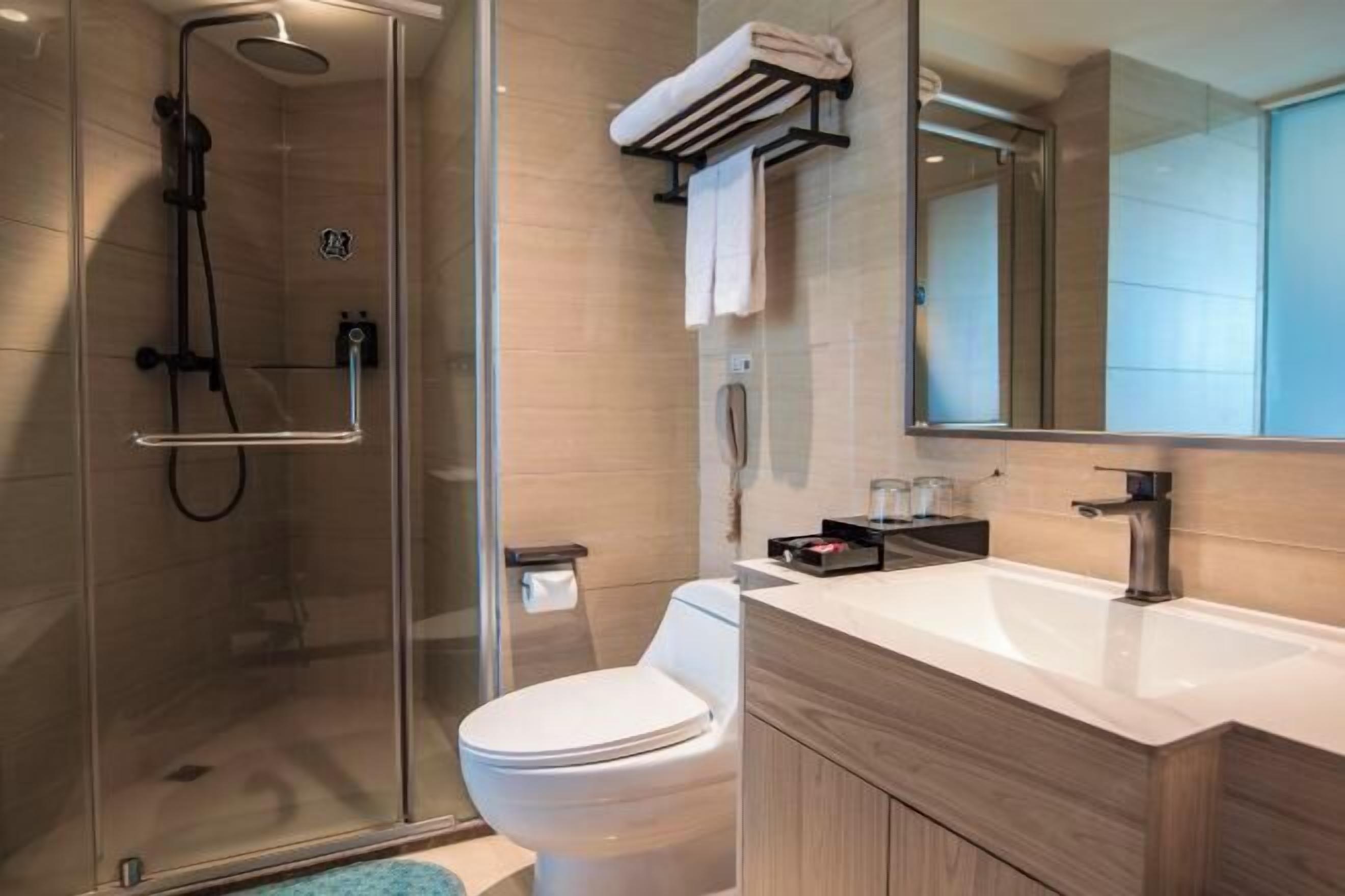 Ein modernes Badezimmer mit einer Glaskabine für die Dusche, einer Toilette, einem Waschbecken mit Spiegel und einem Handtuchhalter.