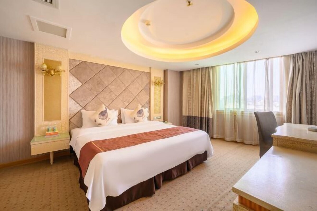 A hotel room with a large bed, a desk, and a view of the city through the window.