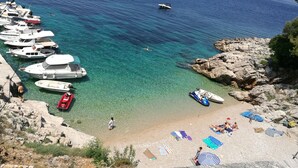 A coastal area with boats docked, a rocky shoreline, and people sunbathing on the beach. - Villa Zvizdan (Makarska)