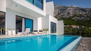 A modern poolside area with a clear view of a mountain range in the background. - Villa Zvizdan (Makarska)