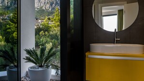A bathroom with a large window, a round mirror, and a yellow vanity. - Villa Zvizdan (Makarska)