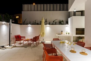 An outdoor patio with a dining table set for six, surrounded by red chairs, a yellow umbrella, and a modern white wall with vertical slats. - Villa Zvizdan (Makarska)