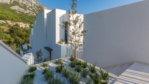 A modern building with a flat roof, a small tree, and a gravel garden. - Villa Zvizdan (Makarska)