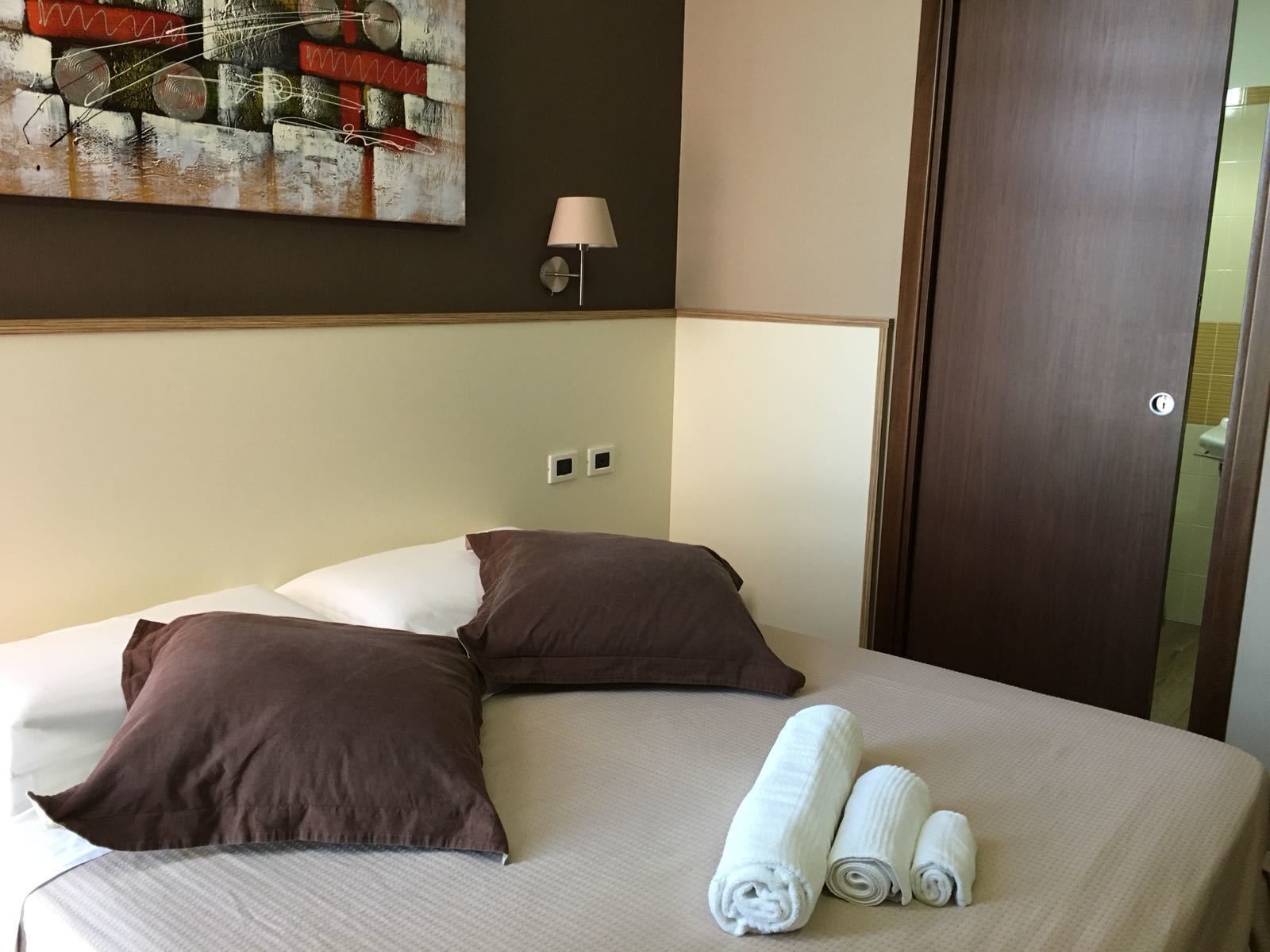 Hotelkamer met een bed, twee kussens, een lamp, een schilderij en een deur.