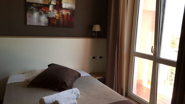 A hotel room with a large bed, a painting on the wall, a lamp, and a window with curtains. - 60Quattro Bedrooms (Lamezia Terme)