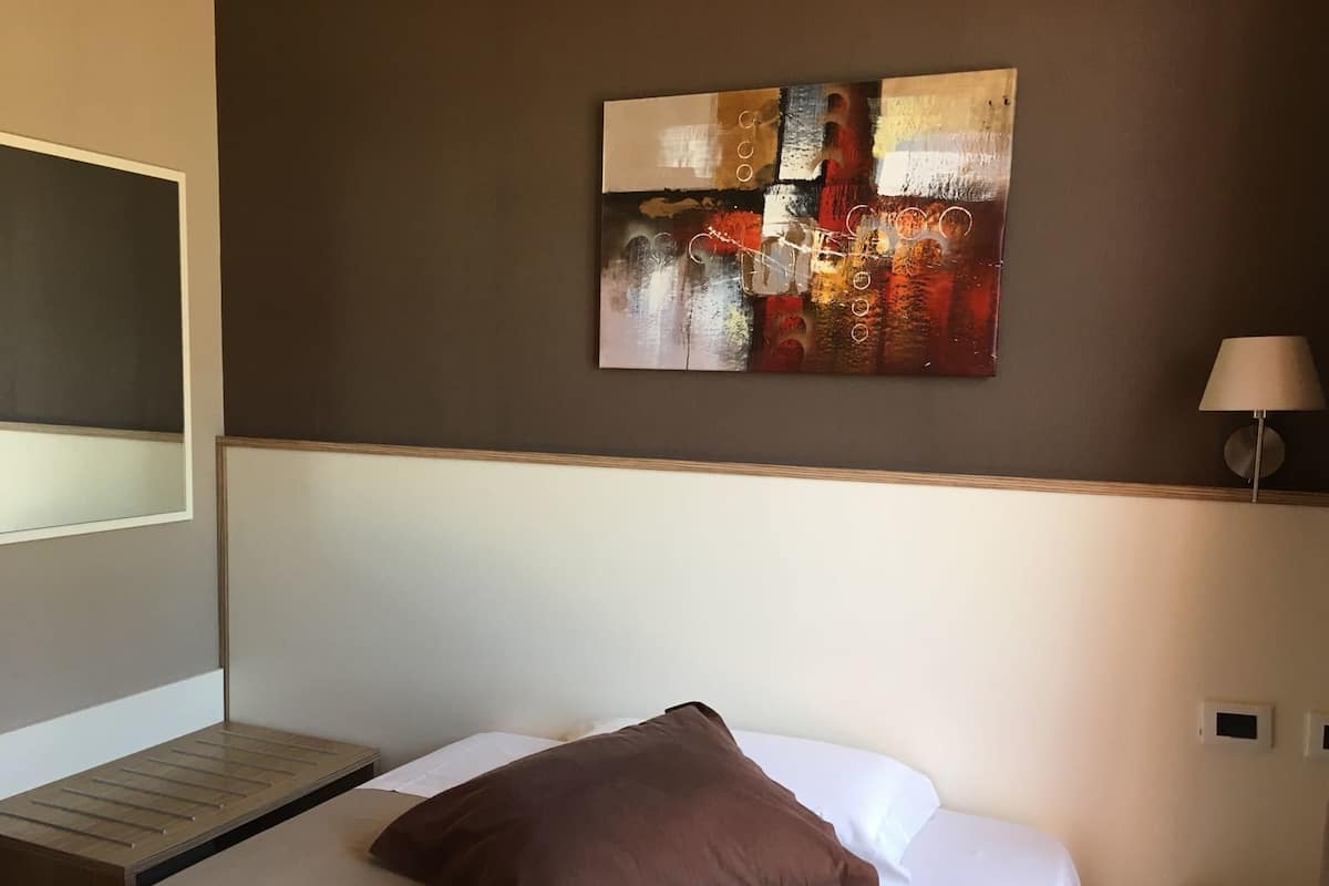 Una habitación de hotel con cama, un cuadro en la pared, una lámpara y una mesita de noche.