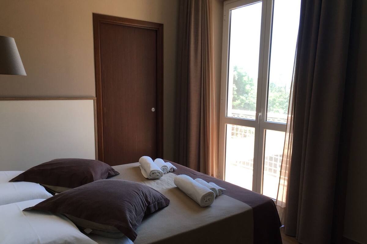 Habitación de hotel con dos camas, una puerta de madera y un ventanal con cortinas.