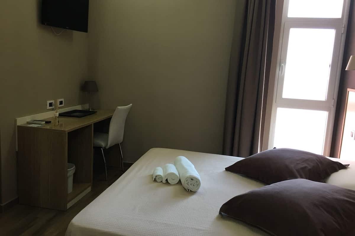 Una habitación de hotel con cama, escritorio, silla, televisor y ventana.