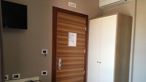 A hotel room with a wooden door, a white wardrobe, a desk with a telephone and papers, and a mounted TV. - 60Quattro Bedrooms (Lamezia Terme)