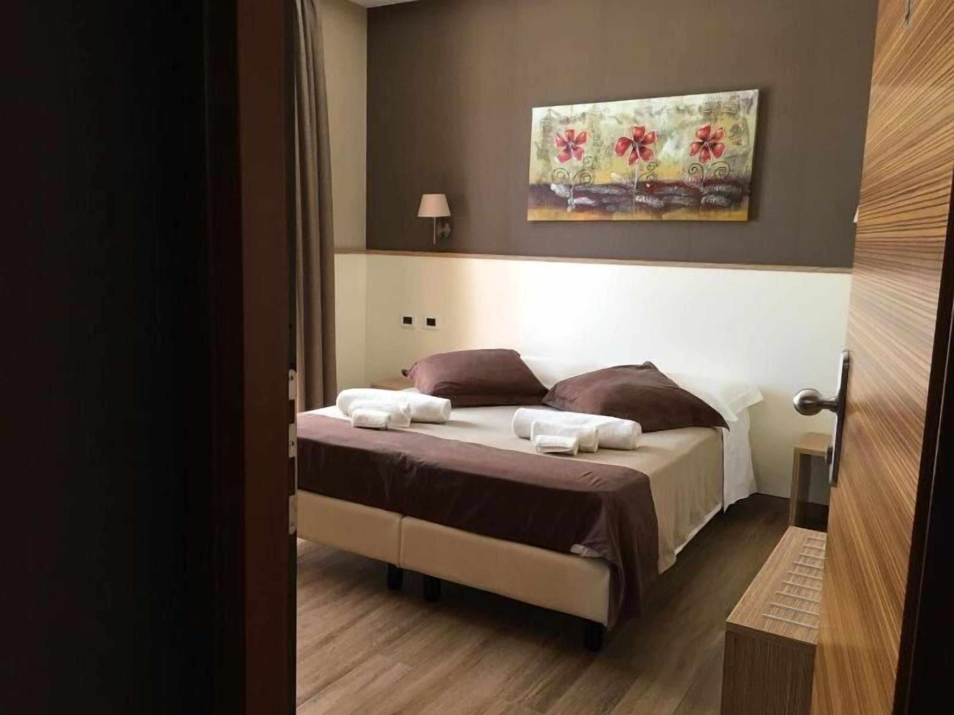 A hotel room with a bed, pillows, a painting on the wall, and a lamp.