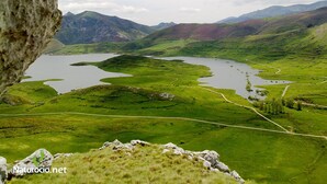Vista panorámica de un paisaje montañoso con un lago y carreteras serpenteantes.
